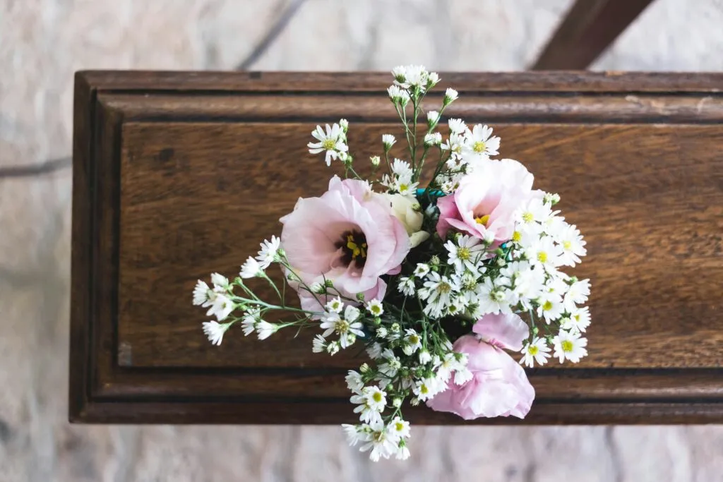 Bouquet de fleurs de deuil roses et blanches posé sur un cercueil en bois massif