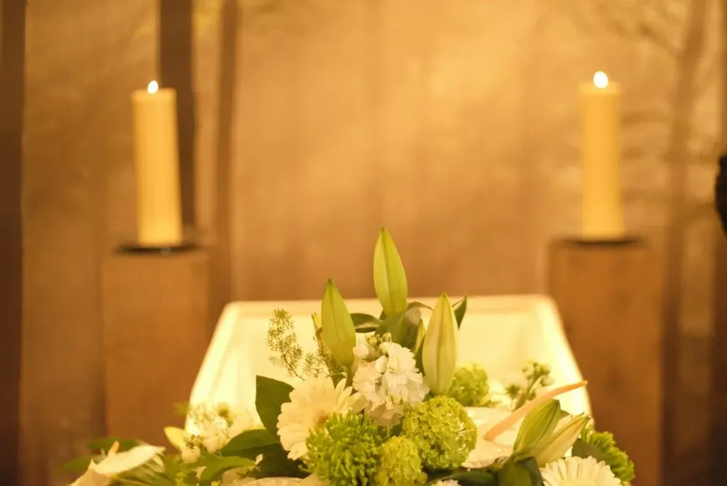 Composition florale funéraire blanche et verte posée devant un cercueil éclairé par des bougies